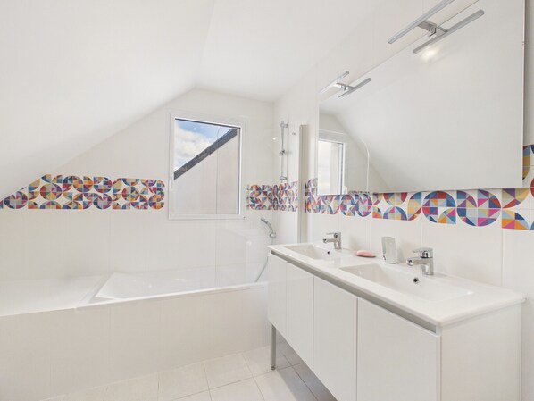 Een moderne badkamer met een bad, een wastafel met twee kommen en een grote spiegel.