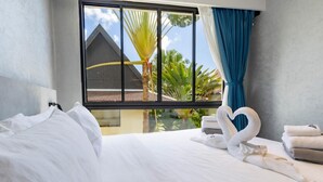 A hotel room with a large window, a bed with white linens, and a heart-shaped towel arrangement. - Beachfront 5122 Building C Modern 2BR Suite (Choeng Thale)