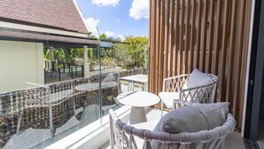 A balcony with a glass railing, a white table, and a wicker chair with a cushion. - Beachfront 5122 Building C Modern 2BR Suite (Choeng Thale)