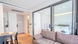 Une chambre d’hôtel moderne, dotée d’un canapé, d’un bureau avec une chaise, d’un lit avec des serviettes soigneusement disposées et d’une grande fenêtre.