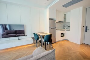A modern living room with a sofa, a dining table, and chairs, a kitchen with a refrigerator and microwave, and a TV mounted on the wall. - Beachfront 257 D One-bedroom Residence (Choeng Thale)