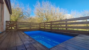 Une terrasse en bois avec une piscine, entourée d’une clôture en bois et d’arbres.