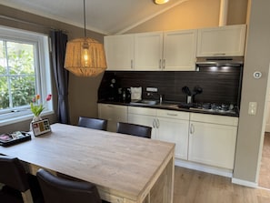 A modern kitchen with white cabinets, a wooden dining table, and a hanging light fixture.