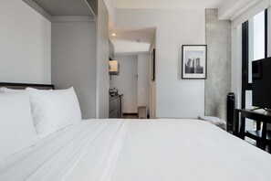Ein Hotelzimmer mit einem großen Bett, einem Schreibtisch, einem Sessel, einem Fernseher und einem Bild an der Wand.
