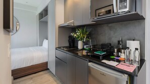 Pieni hotellihuone, jossa on minikeittiö, sänky, peili ja pieni kylpyhuone.
