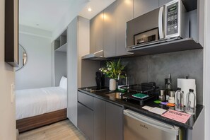 A compact hotel room with a kitchenette, a bed, a mirror, and a small bathroom. - w Inviting Loft in the Heart of Interlomas (Huixquilucan)