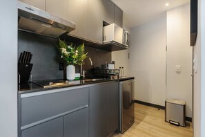 A modern kitchen with grey cabinets, a stainless steel range hood, a built-in microwave, and a small trash bin. - w Inviting Loft in the Heart of Interlomas (Huixquilucan)