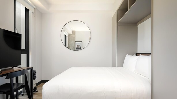 Moderni hotellihuone, jossa on suuri sänky, televisio ja pyöreä peili seinällä.