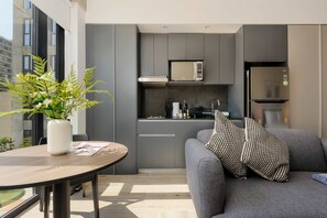 A modern kitchen with grey cabinets, a microwave, and a refrigerator. There is a grey sofa with patterned cushions and a table with a vase of flowers. - w Sleek Loft in the Heart of Interlomas (Huixquilucan)