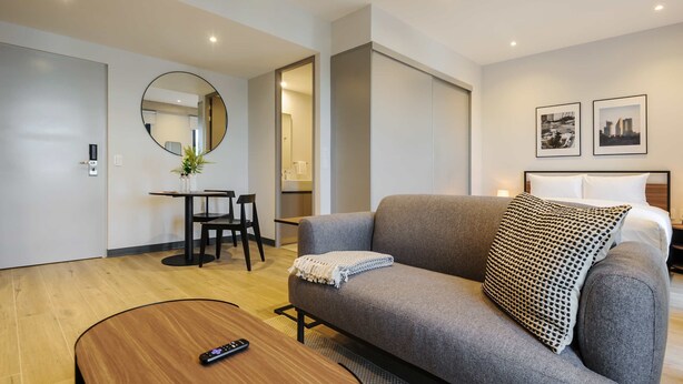 A modern hotel room with a grey sofa, a round mirror, a small dining table with chairs, and a wooden coffee table. - w Appealing Loft in the Heart of Interlomas (Huixquilucan)