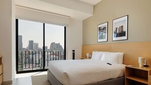 A modern hotel room with a large bed, a nightstand, a bedside table, and a city view through a large window. - w Deluxe Loft w/ Balcony in Tabacalera (Mexico City)