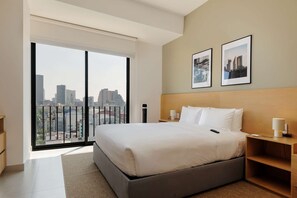 A modern hotel room with a large bed, a nightstand, a bedside table, and a city view through a large window. - w Deluxe Loft w/ Balcony in Tabacalera (Mexico City)