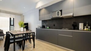 A modern kitchen with dark cabinetry, a built-in microwave, and a dining area with a table and chairs. - w Amazing 1BR in the Heart of Interlomas (Huixquilucan)