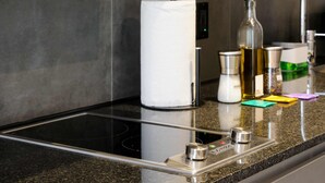 A kitchen with a built-in induction cooktop, a paper towel holder, a bottle of olive oil, and a set of colorful cleaning cloths.