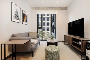 Un salon moderne avec un canapé, une table basse, un pouf, un téléviseur et des œuvres d’art accrochées au mur.