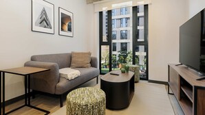 A modern living room with a grey sofa, a small table, a patterned ottoman, and a flat-screen TV.