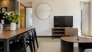 A modern living room with a dining area, a large mirror, a flat-screen TV, and a kitchen visible in the background. - w Luxurious 2BR in the Heart of Interlomas (Huixquilucan)
