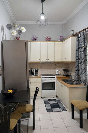 A compact kitchen with a dining area, featuring a refrigerator, stove, sink, and a dining table with chairs. - Zografou Cozy Apartment in the heart of Athens! (Zografou)