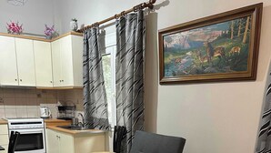 A compact living space with a sofa bed, kitchenette, and a painting on the wall. - Zografou Cozy Apartment in the heart of Athens! (Zografou)