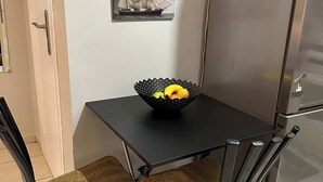 A small dining area with a black table, two chairs with woven seats, and a black bowl with fruits. A framed picture of a ship is on the wall. - Zografou Cozy Apartment in the heart of Athens! (Zografou)