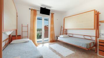 Un dormitorio con dos literas, un televisor montado en la pared, un balcón con cortinas anaranjadas y una puerta corredera de vidrio.
