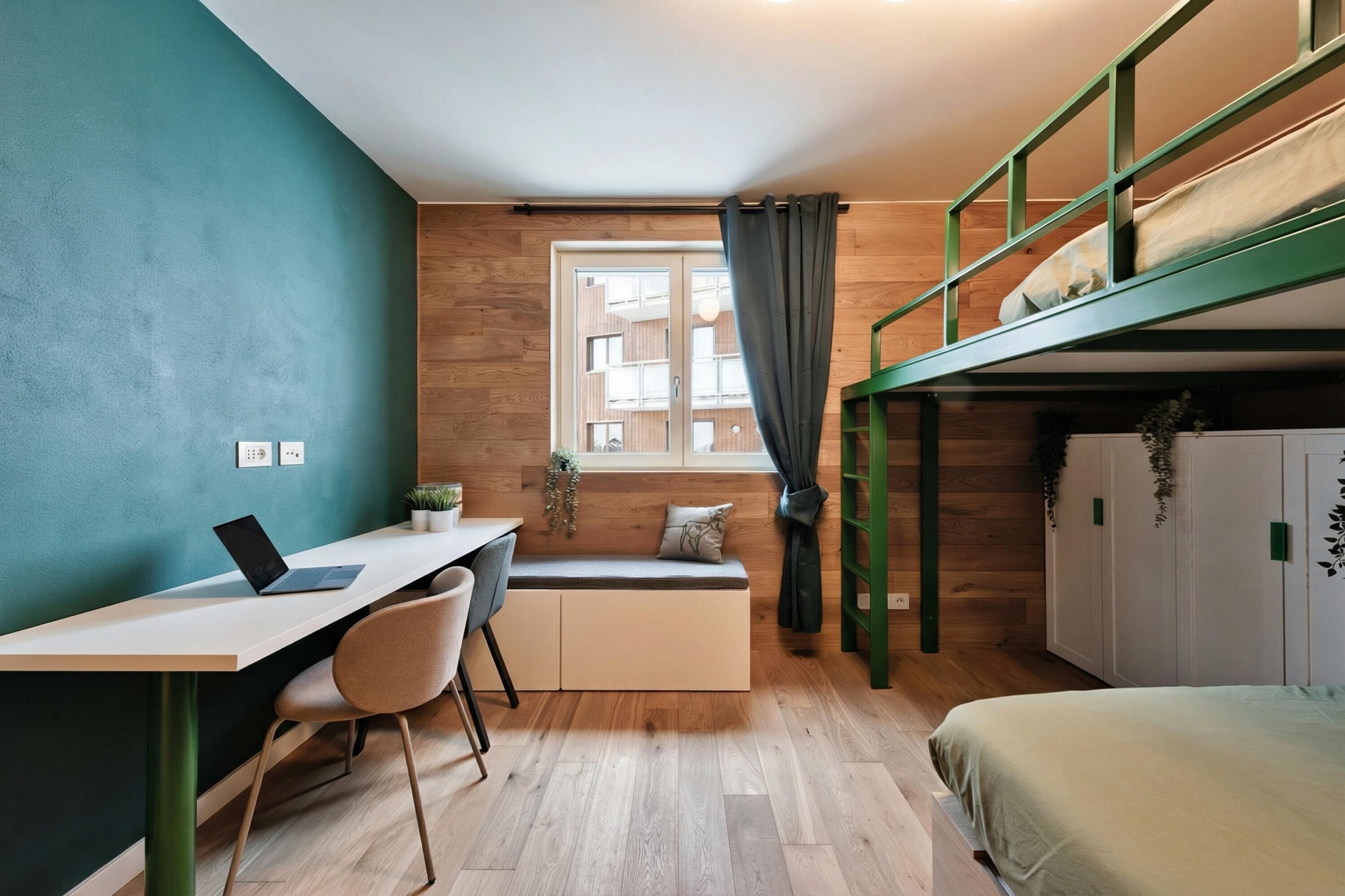 A compact room with a bunk bed, a desk with a laptop, a chair, and a window with curtains.