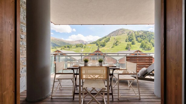 Eine Holzterrasse mit Tisch und Stühlen, mit Blick auf eine gebirgige Landschaft.
