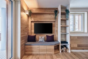 Ein modernes Interieur mit einer Holzwand, einem Flachbildfernseher, einer Bank mit Kissen und einer Pflanze.