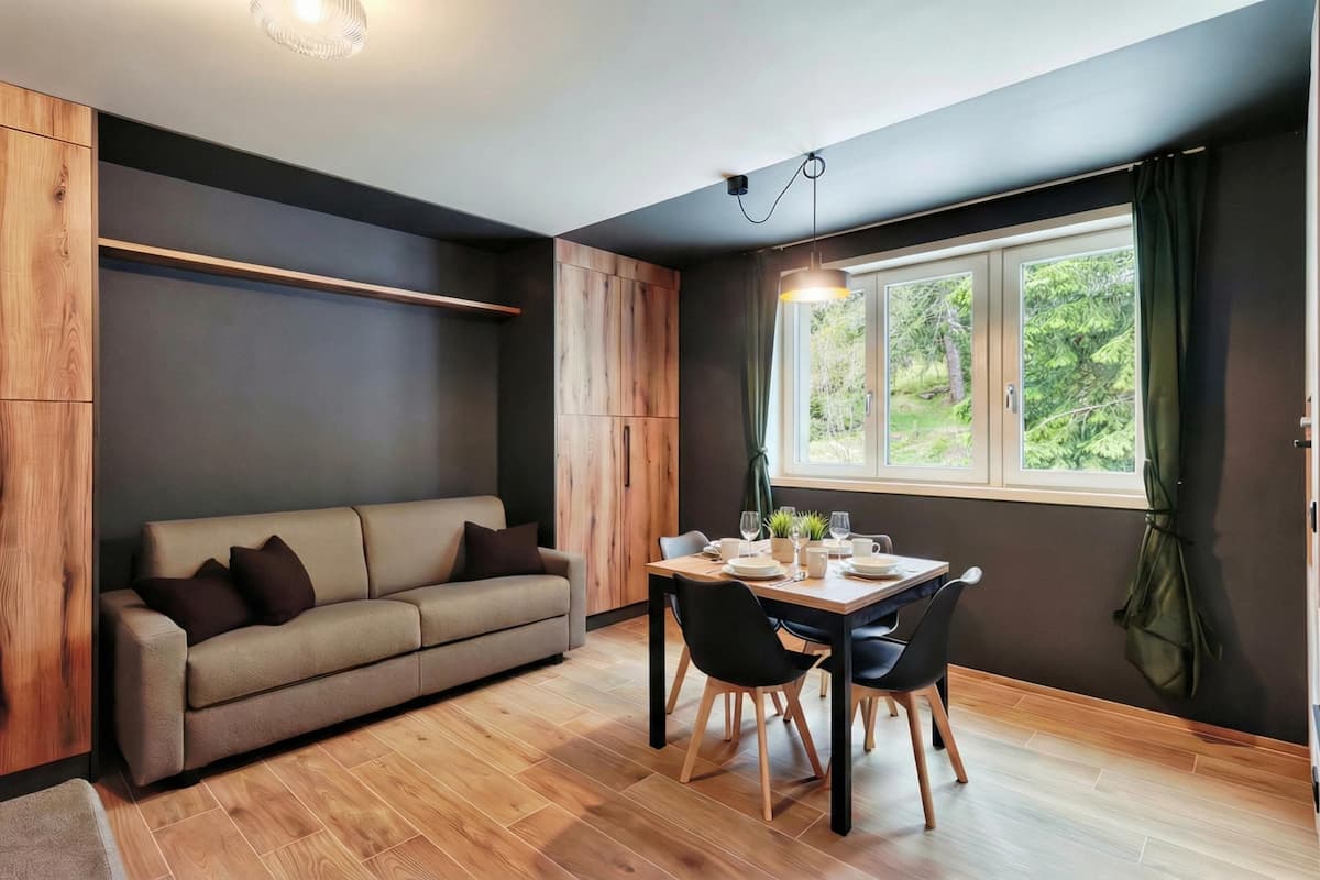 A modern room with a sofa, dining table, chairs, and a window with curtains.