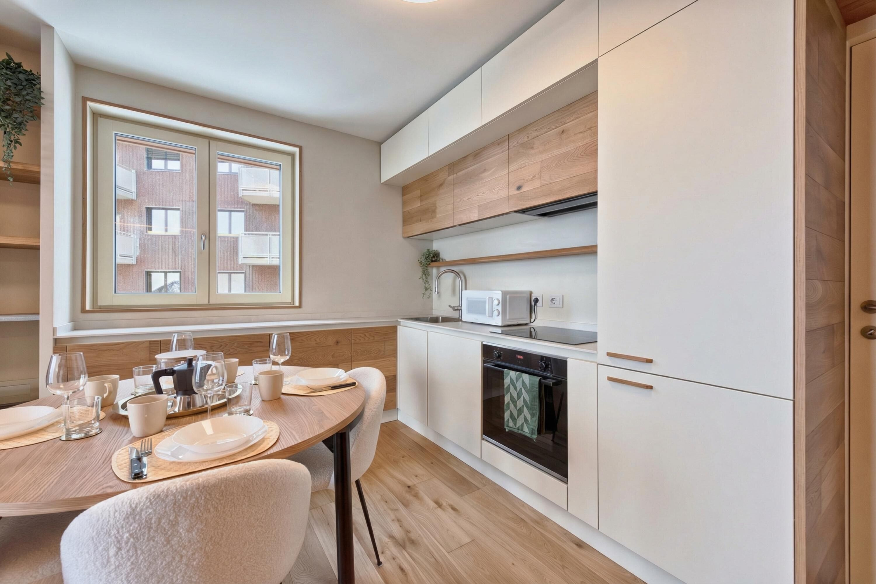 Una cocina moderna con armarios blancos, un microondas y una estufa. Hay una mesa de comedor puesta con platos, vasos y cubiertos.