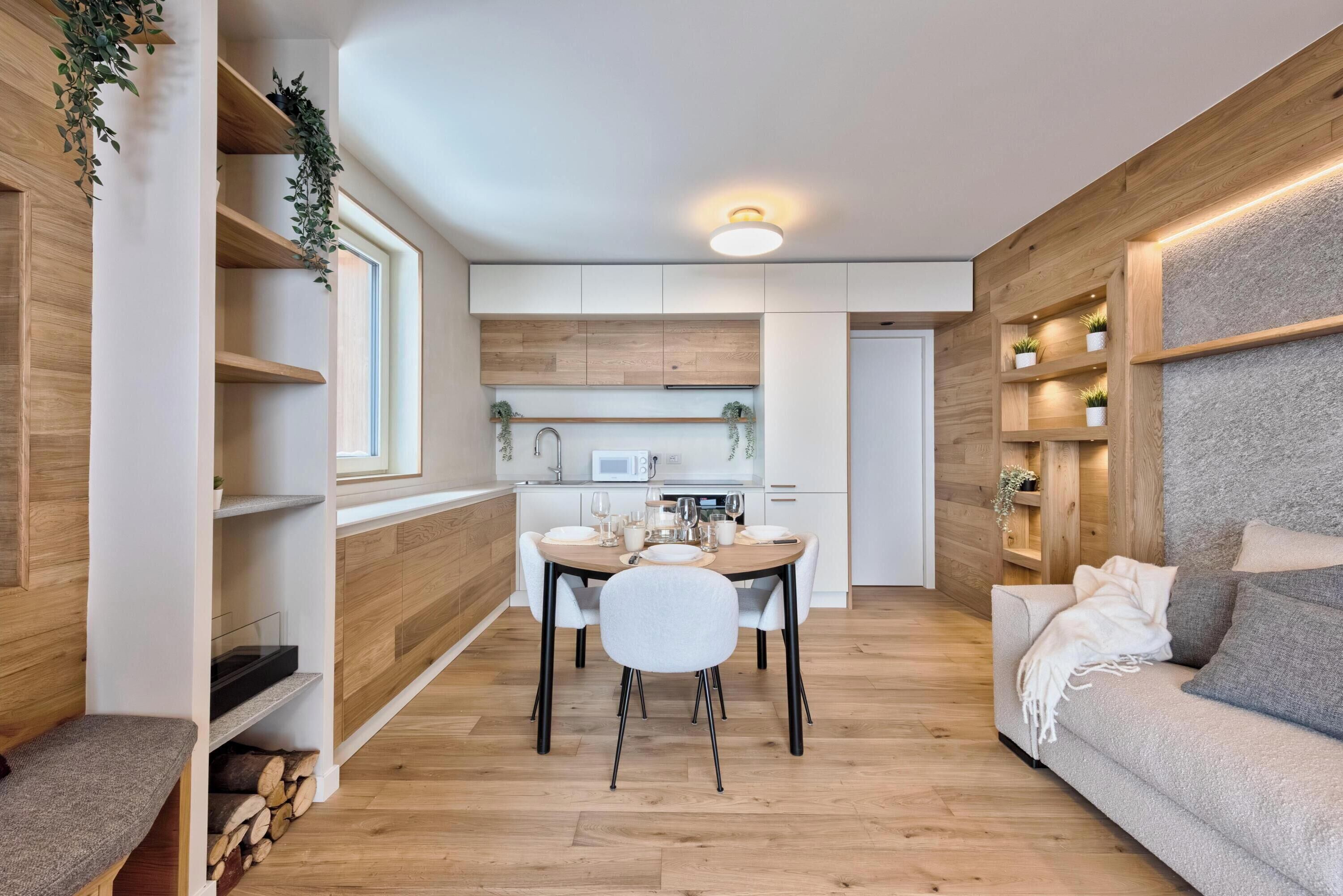 A modern kitchen with white cabinets, a dining table with chairs, and a sofa.