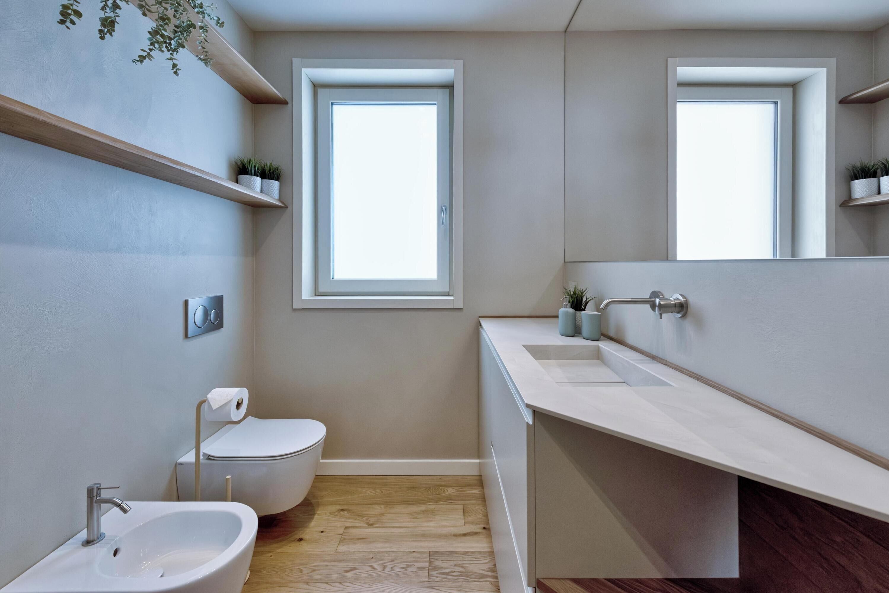Egy modern fürőszoba, amelyben WC, bidé, mosdókagyló és tükör található. Két ablak biztosítja a természetes fényt.
