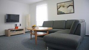 Una sala de estar moderna con un sofá gris, una mesa de centro de madera, un televisor de pantalla plana y un cuadro en la pared.