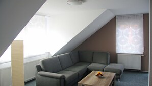 Una sala de estar moderna con un sofá modular gris, una mesa de centro de madera y un ventanal con cortinas de gasa.