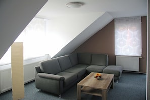 A modern living room with a grey sectional sofa, a wooden coffee table, and a window with sheer curtains. - Apartments am Grafenberg - spacious vacation homes and apartments (Grafenberg)