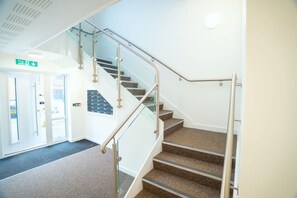 Ein modernes Interieur mit einer Treppe, einem Brandschutztürschild und einer wandmontierten Bedienkonsole.