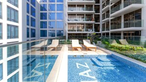 A modern indoor pool with glass walls, lounge chairs, and a view of high-rise buildings. - Stayshort - Elegant Studio Living in JVC Perfect for 2 (Dubai)