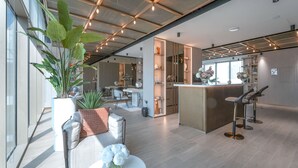 A modern hotel lobby with a central bar area, seating arrangements, and large windows allowing natural light. - Stayshort - Elegant Studio Living in JVC Perfect for 2 (Dubai)