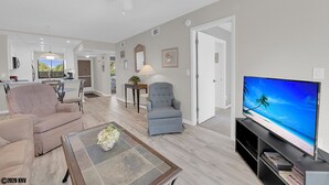 Ein modernes Wohnzimmer mit einem Flachbildfernseher, einem beigefarbenen Sofa, einem blauen Sessel und einem Couchtisch mit einer Vase.