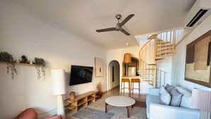 Ein modernes Wohnzimmer mit einer Couch, einem Couchtisch und einem Fernseher. Eine Treppe führt zu einer erhöhten Ebene.