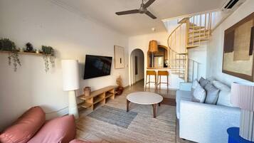 Un salon moderne avec un canapé, une table basse et un téléviseur. Un escalier mène à un niveau supérieur.