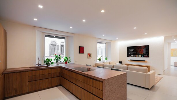 A modern kitchen with a large island, wooden cabinets, and a built-in oven. There is a dining area with a sofa and a flat-screen TV mounted on the wall. - Lussuosa residenza nel centro di Verona (Verona)
