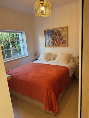 Quarto com cama, janela, pintura e luminária suspensa.