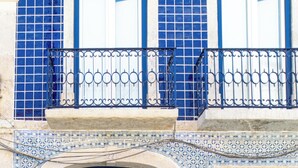 Un edificio con puerta azul, balcón con barandilla de metal y fachada de azulejos.
