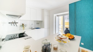 Una cocina moderna con armarios blancos, una estufa negra y una encimera con un frutero, una jarra y frascos.