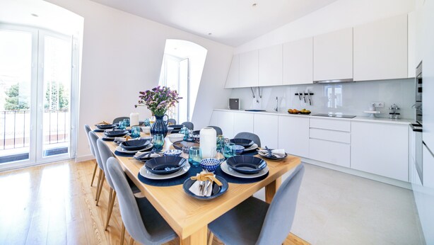 Una cocina moderna con armarios blancos, una mesa de comedor de madera dispuesta con platos azules y blancos, y un florero con flores.