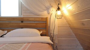 Un dormitorio con cabecera de madera, cama con ropa de cama blanca, lámpara colgante y ventana con cortinas translúcidas.