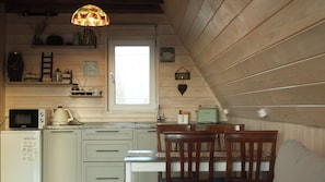 Une cuisine chaleureuse avec des murs en bois, une fenêtre, un four à micro-ondes, une bouilloire et une table à manger avec des chaises.