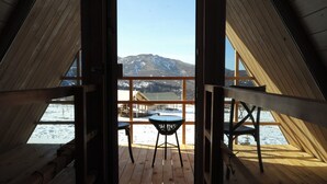 Una terraza de madera con mesa y sillas, con vista a un paisaje nevado y montañas.