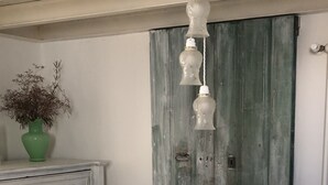 Une table à manger blanche ornée d’un panier tressé au centre, des chaises blanches, un vase vert contenant des fleurs séchées, et une porte en bois rustique en arrière-plan.